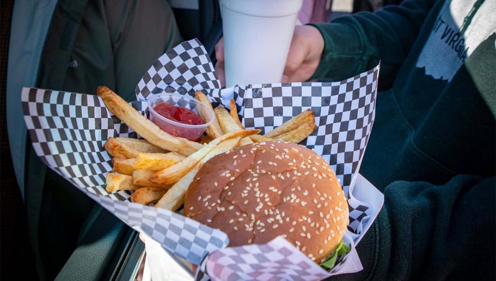 A burger with lettuce and fries served in a checkered paper basket, accompanied by a small cup of ketchup at Jim's Drive-In.