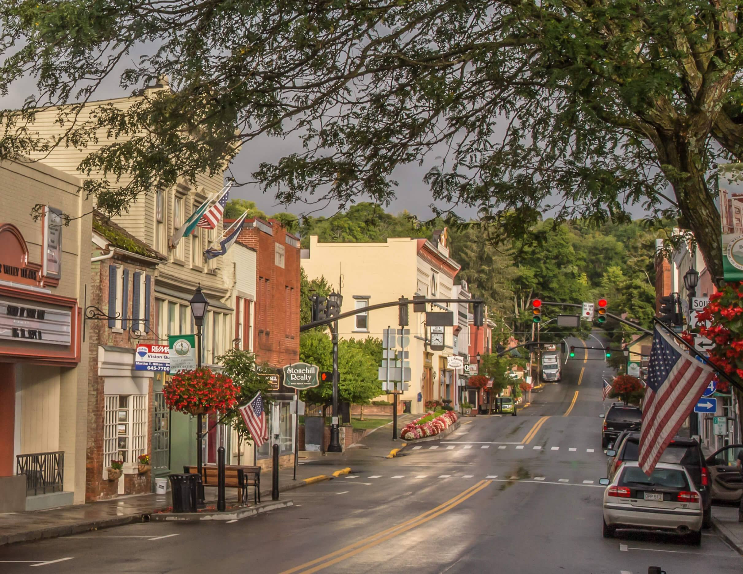 Small-town Main Street in Lewisburg, WV, with historic buildings, American flags, and flower baskets after a rain.
